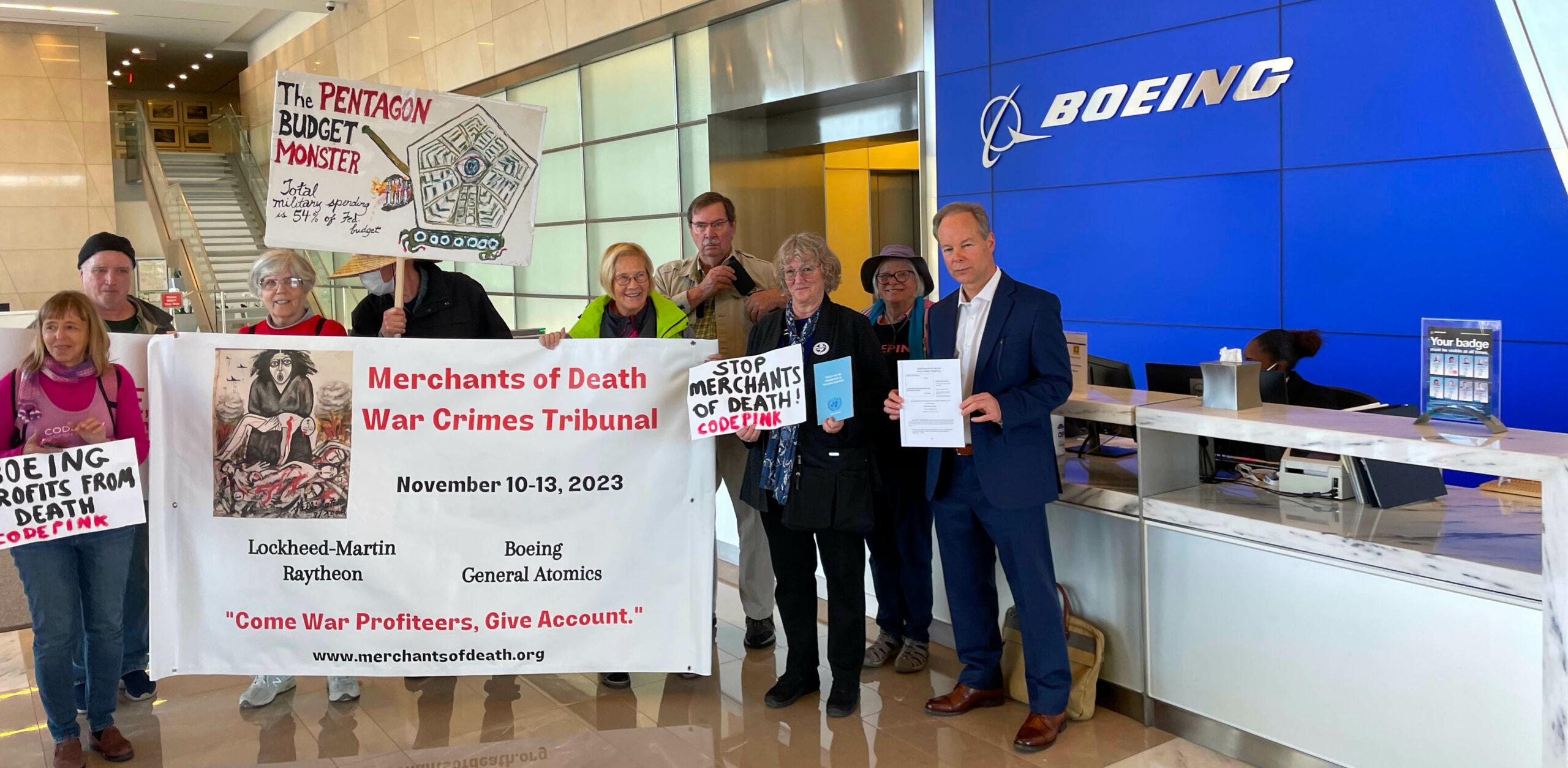 Members and supporters of the Merchants of Death War Crimes Tribunal hold anti-war signs and hold the subpoena in front of the Boeing office front desk